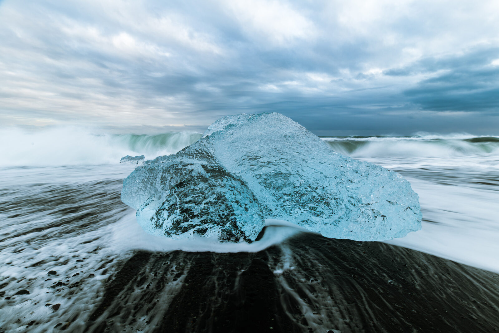 A block of glacier ice on the black sand as a wave washes around it
