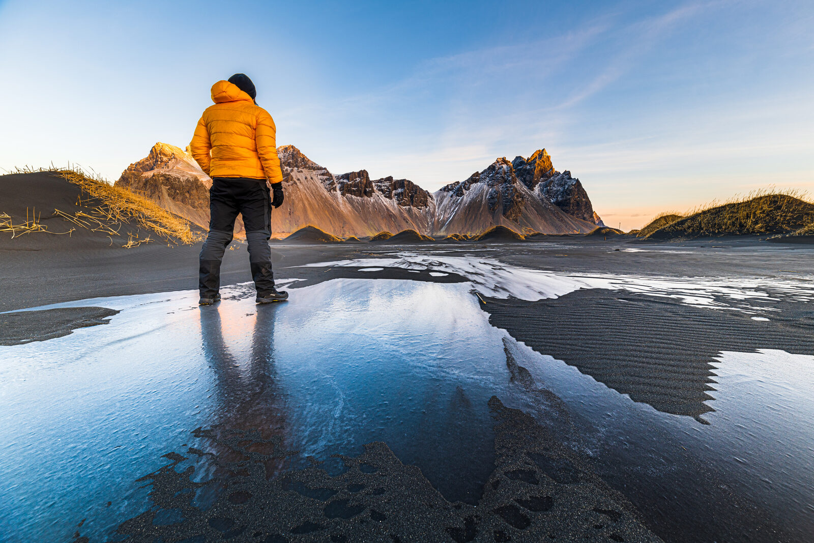 Danni in a yellow jacket standing on the frozen sand, looking at Vestrahorn